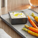 An Acopa matte grey and black square melamine sauce cup with white dip next to a plate of food with carrots.