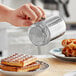 A person using a Choice stainless steel shaker to sprinkle powdered sugar on waffles.