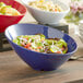 A blue Acopa melamine bowl filled with salad on a table.