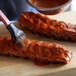 A person uses a paint brush to brush Frank's RedHot sauce on ribs.