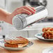 A hand using a silver stainless steel shaker to pour powder on waffles on a plate.