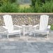 Two white Flash Furniture Charlestown folding Adirondack chairs with a white table on a stone patio.