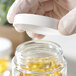 A hand in gloves holding a 53/400 white plastic cap over a clear jar.