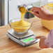 A person weighing corn flour in a bowl on an AvaWeigh stainless steel digital portion scale.