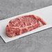 A piece of raw Rastelli's USDA Prime New York Strip Steak on a white surface.