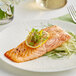 A Rastelli's Faroe Island salmon fillet on a white plate with lemon and herbs.