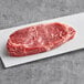 A piece of Rastelli's wet-aged New York strip steak on a white surface.