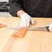 A person wearing a white glove using a Victorinox Slicing/Salmon Knife to cut a piece of salmon on a cutting board.