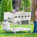 A woman standing next to a Backyard Pro stainless steel outdoor grill with food on it.