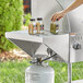 A person pouring liquid into a white cylinder on a Backyard Pro stainless steel end shelf on a grill.