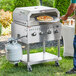 A man using a Backyard Pro pizza oven attachment to cook a pizza on a grill.