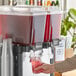 A person pouring Tractor Beverage Co. Organic Hibiscus Concentrate into a beverage dispenser.
