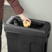 A person using a yellow glove to put a yellow crumpled paper in a Toter Slimline trash can.