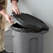 A man putting a black Toter lid on a round trash can.