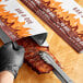 A gloved hand uses a barbecue tong to hold a foil bag of BBQ ribs.