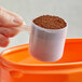 A hand using a 70 cc polypropylene scoop to pour coffee powder into a container.