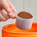 A hand using a 94 cc Polypropylene scoop to pour brown powder into a container.