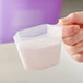 A hand holding a 4 oz. polypropylene measuring cup with white powder.