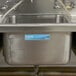 A school kitchen sink with Noble Products permanent labels for water, rinse, and sanitize.