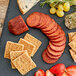 A platter of Shaffer Venison Farms Smokey Barbecue Wild Boar Summer Sausage with cheese, crackers, and fruit.