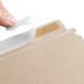 A person using a finger to open a Lavex Stayflats Kraft mailer with a white strip.