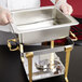 A person holding a stainless steel water pan for a Vollrath Classic Brass chafer.
