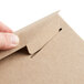 A hand opening a brown Lavex Stayflats rigid mailer box with a paper clip.