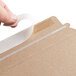 A hand using tape to seal a Lavex Stayflats Kraft mailer.