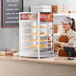 A woman standing behind a bakery counter with a ServIt countertop display warmer full of pizza.