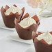 Three chocolate brown tulip cupcakes in Enjay wrappers on white plates.