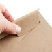A hand opening a Lavex Stayflats Kraft Rigid Mailer with a paper clip.