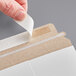 A person's finger peeling back white self-sealing tape on a paper.