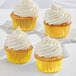 A group of Enjay gold foil cupcake liners with a cupcake with white frosting.