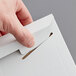 A person opening a Lavex Stayflats white rigid mailer with a paper clip.