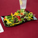 A black Fineline plastic salad plate with salad and a fork on a table.