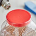 A person uses a drill to add a 1" clear non-perforated shrink band to a plastic container with a red lid.
