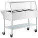 A ServIt stainless steel electric steam table on wheels with angled glass sneeze guard.