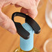 A hand using a Franmara black foil cutter to open a wine bottle on a counter.