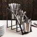 A black steel Cal-Mil vertical rack with metal cups holding silverware.