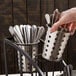 A hand holding a Cal-Mil vertical black steel flatware display with silver spoons.
