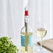 A bottle of white wine with a Franmara Acrylic Wine Pourer / Chiller Stick in a glass on a table.