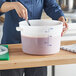 A woman mixing purple liquid in a large white Vigor food storage container.