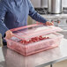 A woman in a blue jacket opening a Carlisle red plastic food storage container full of raw meat.