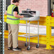 A man in a safety vest standing next to a Lavex Stainless Steel Locking Mobile Receiving Desk cart.
