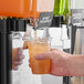 A person using Pure Craft Beverages Orange Passionfruit beverage concentrate to fill a plastic cup with green liquid.