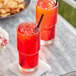 Two glasses of Pure Craft Beverages fruit punch with straws on a table with food.