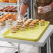 A person in a white apron holding a yellow MFG Fiberglass tray of cupcakes on a counter.