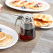 A Tablecraft glass syrup dispenser on a table with a plate of pancakes.