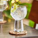A Libbey gin and tonic glass with ice and lime on a coaster.