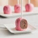 A Chalet Desserts chocolate cake pop with pink frosting on a white stick on a white plate.